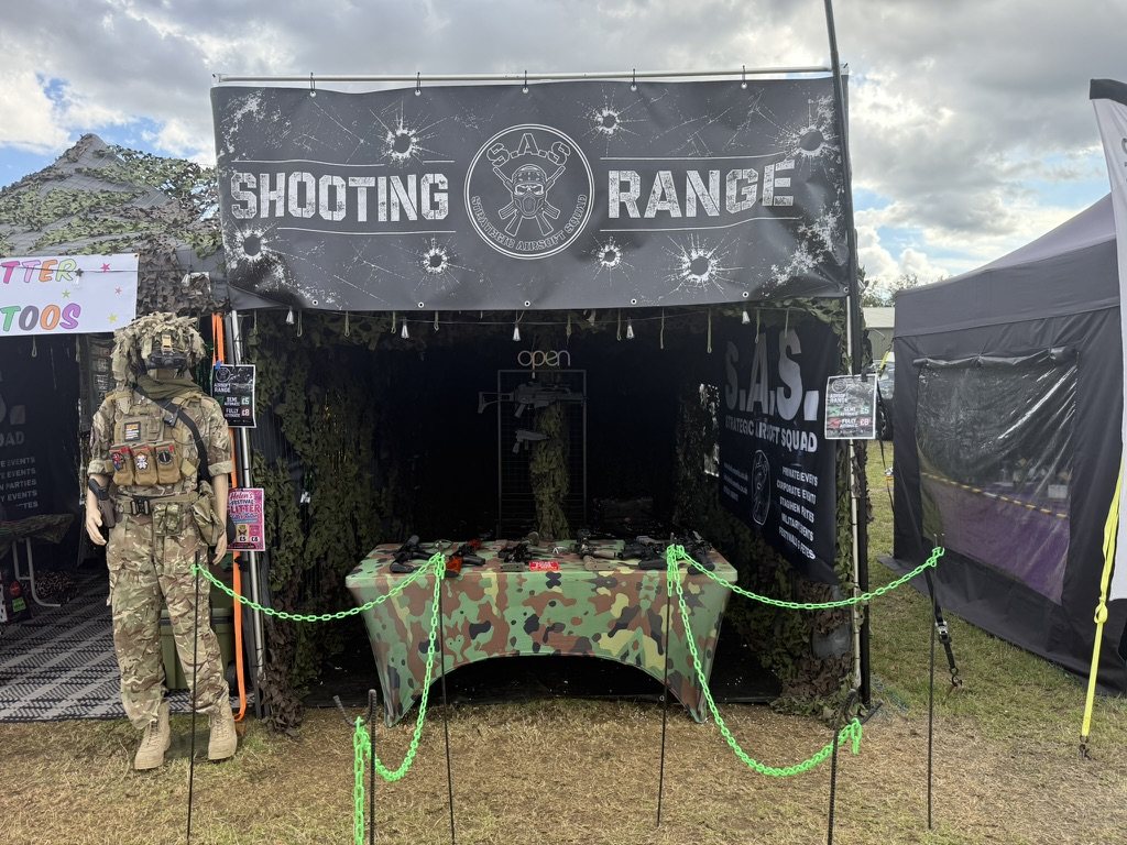 The S.A.S. mobile airsoft shooting range set up at an outdoor show, camouflage netting and banner overhead